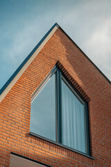 Obraz premium Close-up view of a modern house with a triangular brick wall and large glass window, highlighting contemporary architecture and design against the sky.