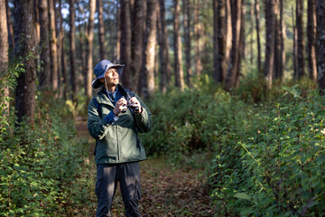 Bird watcher is looking through binoculars while exploring in the pine forest for surveying and...