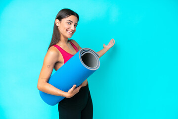 Young sport caucasian woman going to yoga classes while holding a mat isolated on blue background...