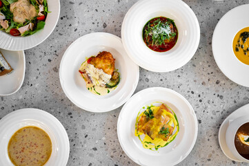 A top-down view of an elegant table set with various gourmet dishes, including soups and entrees, showcasing vibrant colors and artistic plating against a textured background.