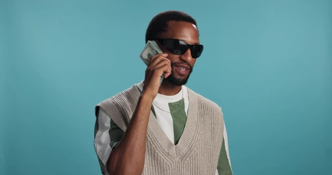 Happy, black man and sunglasses with money call for pimping, rapping or financial freedom on a blue studio background. Male person, rapper or cool model with smile, bills or cash for wealthy chat