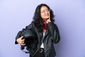 Young asian woman with a motorcycle helmet isolated on purple background thinking an idea while looking up