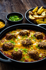 Cowboy meatballs baked with cheddar cheese in frying pan on wooden table