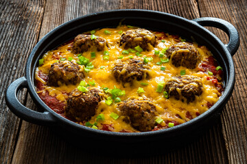 Cowboy meatballs baked with cheddar cheese in frying pan on wooden table