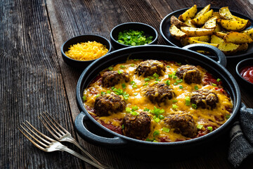 Cowboy meatballs baked with cheddar cheese in frying pan on wooden table