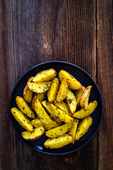 Baked potato wedges with spices and herbs on wooden table