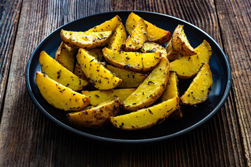 Baked potato wedges with spices and herbs on wooden table