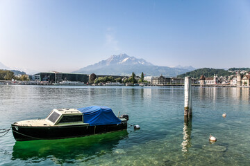 the city of lucerne in switzerland with pilatus mountain in the background. A small boat with a blue cover is floating in the water