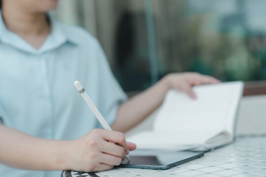 Freelancer using digital stylus on tablet at outdoor café table with notebook. Woman remote work, creativity, digital business and modern work-from-home productivity in relaxed environment.
