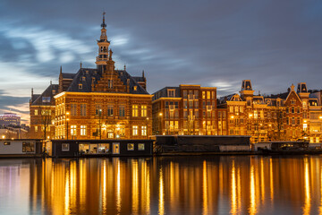 Fototapeta premium Amsterdam in the evening, houseboats and historical buildings mirrored in Amstel river after sunset
