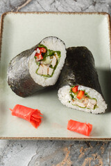 Japanese Mexican sushirrito with rice, chicken, cream cheese, vegetables and lettuce close-up in a plate on the table. Vertical