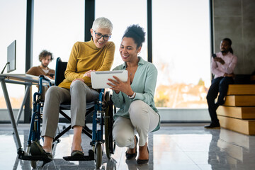 Disabled woman in wheelchair looking at computer, discussing startup project with interracial team