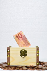 Vertical shot. Close up, ten euro bill in wooden box and coins scattered around, savings concept. 