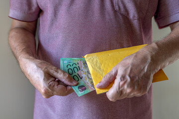 Close-up on a man's hand taking or placing a bundle of one hundred Australian dollar notes into an envelope. Concept illustration for bribing, corruption or cash payment.