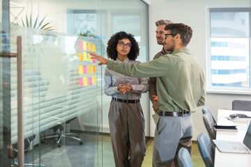 Obraz premium Businesspeople talking in their diverse team during a brainstorming session with sticky notes on glass wall in a modern office