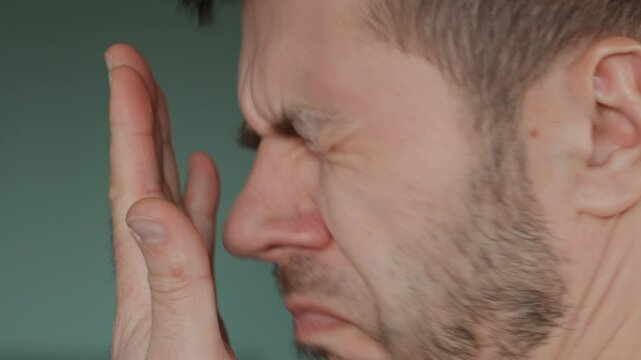 Bad breath from mouth. Close-up of man checking his breath by exhaling into his hand, showing concern about oral hygiene or bad breath
