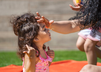 Mother applying sunscreen lotion to her daughter's forehead on a sunny summer day