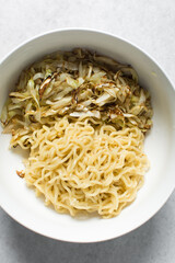 overhead view of a bowl of ramen with cucumber and cabbage slices, top view of noodles bulked with cabbage and cucumber in grey bowl	