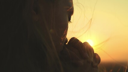 girl prays looking sunset, long hair flying away in glare sunlight rays strong wind, looking at...