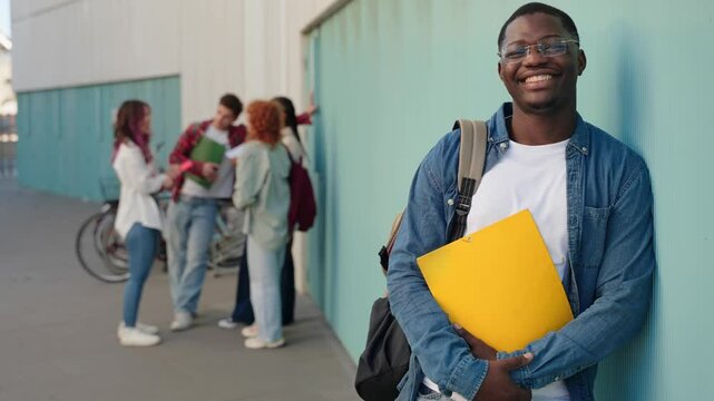 Young African American male University student standing with classmates talking holding backpack looking at the camera and smiling 