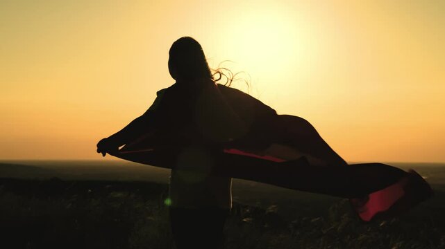 girl superhero with long hair red cape wind sunset. brave superhero ready help. superhero background sky rays sun. childhood dream teenager. child stretches hands sun. happy childhood superhero game