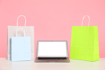 Internet shopping. Laptop and colorful paper bags on table against pink background