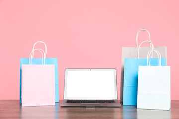 Internet shopping. Laptop and colorful paper bags on wooden table against pink background