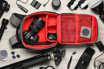 Professional photographer's equipment and backpack on light wooden background, flat lay