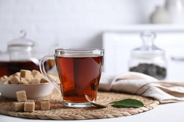 Aromatic black tea in cup and brown sugar cubes on white table
