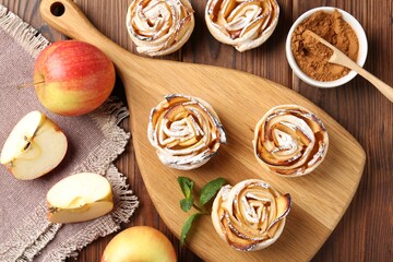 Tasty apple roses with powdered sugar served on wooden table, flat lay