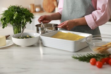 Woman making spinach lasagna at marble table indoors, closeup