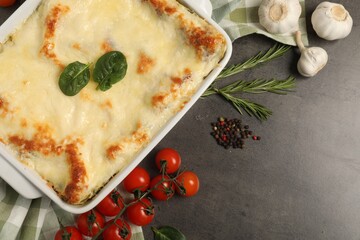 Delicious spinach lasagna in baking dish and ingredients on grey table, flat lay. Space for text