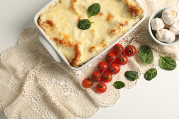 Delicious spinach lasagna in baking dish and ingredients on white table, flat lay
