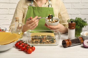 Woman making spinach lasagna at white wooden table indoors, closeup
