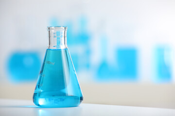 Conical flask with blue liquid on table indoors, closeup. Space for text
