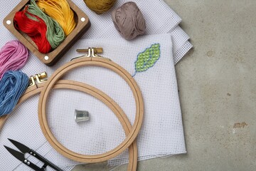 Embroidery and different sewing accessories on grey table, flat lay. Space for text