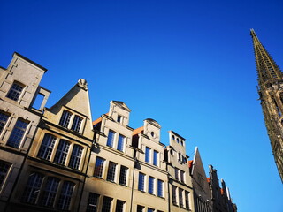 Obraz premium Schöne alte Giebelhäuser vor blauem Himmel bei Sonnenschein am Prinzipalmarkt mit dem Kirchturm der römisch-katholischen Kirche St. Lamberti in der Altstadt von Münster in Westfalen im Münsterland