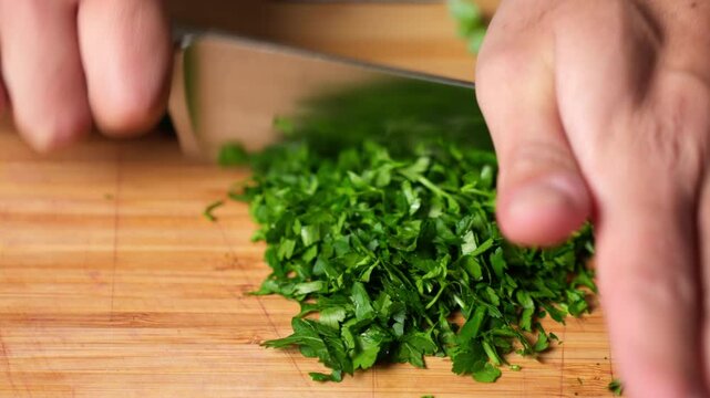 Home chef chopping and cutting parsley herbs on a wooden cutting board with a kitchen knife. cooking concept.
