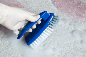 Blue brush on the floor and much foam with hand in rubber glove. Cleaning.