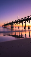 Obraz premium Pier at Dusk: Serene Coastal Sunrise Under a Wooden Jetty, Ocean Reflection, Beautiful Sunrise Aesthetic.