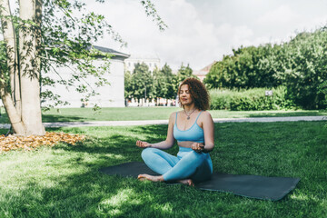 Beautiful athletic barefoot woman practicing yoga in park in summer morning, meditating in lotus...