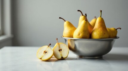 A bowl of ripe, yellow pears sits on a pristine white surface, accompanied by two perfectly halved pears, showcasing their juicy, sweet interiors.
