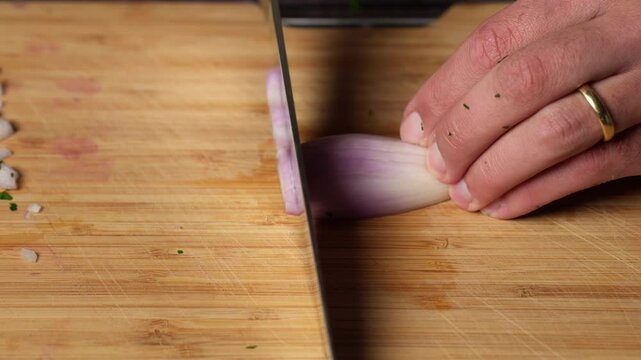 Home chef cutting shallot on a wooden cutting board with a kitchen knife. cooking concept.