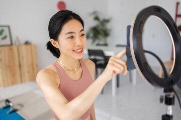Young asian female trainer preparing streaming fitness video class from home. Content creator people concept.