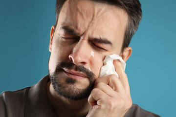 Sad man with paper tissue crying on light blue background