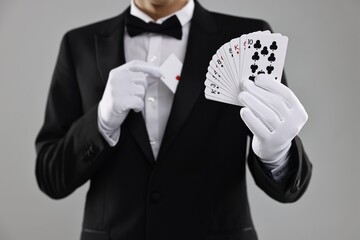 Illusionist hiding one playing card behind jacket lapel while showing deck on grey background