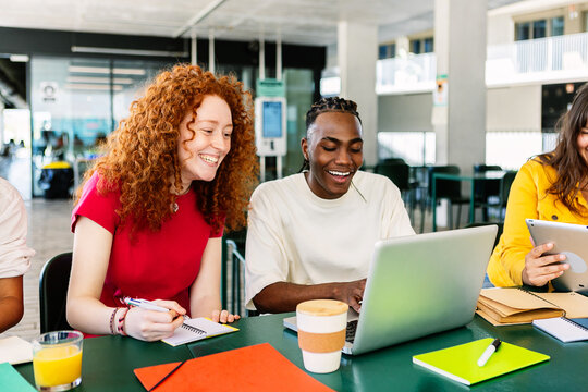 Diverse group of college students studying together at university cafeteria. Happy classmate friends talking while preparing exam or doing group work sitting on bar table outside. Education concept.