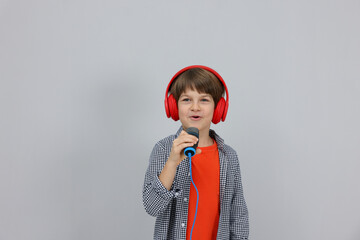 Cute boy with microphone in headphones singing near grey wall. Space for text