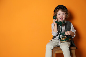 Cute little boy with old telephone on stool against orange background, space for text © New Africa