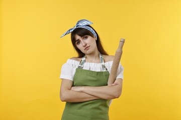 Upset woman with rolling pin on yellow background